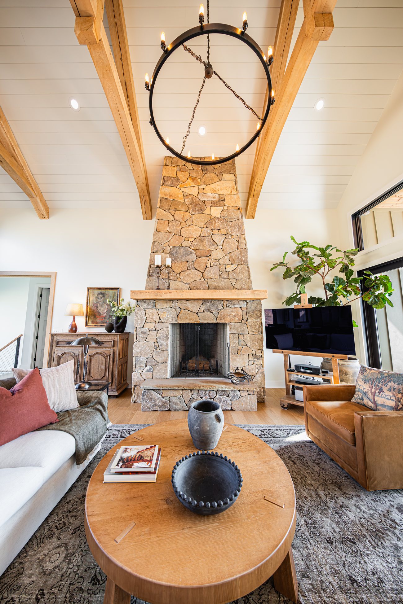 The great room at Mountain Craftsman, with a stone fireplace under exposed timber trusses